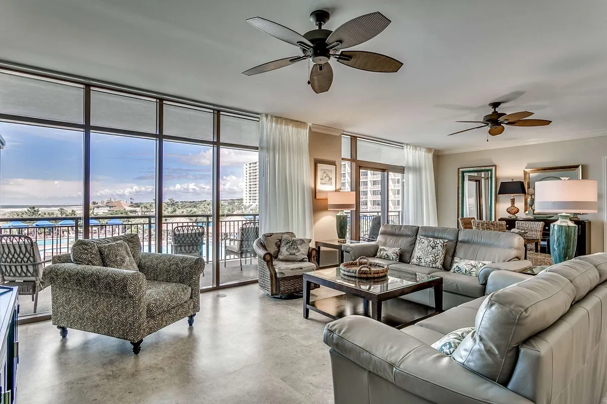 This inviting condo living area features plush, comfortable seating arranged around a stylish coffee table, all bathed in natural light from expansive windows that open up to sweeping ocean views. The space effortlessly blends indoor relaxation with the promise of stunning sunsets and the soothing sounds of the Atlantic, creating an ideal setting for family gatherings or peaceful moments with a view.