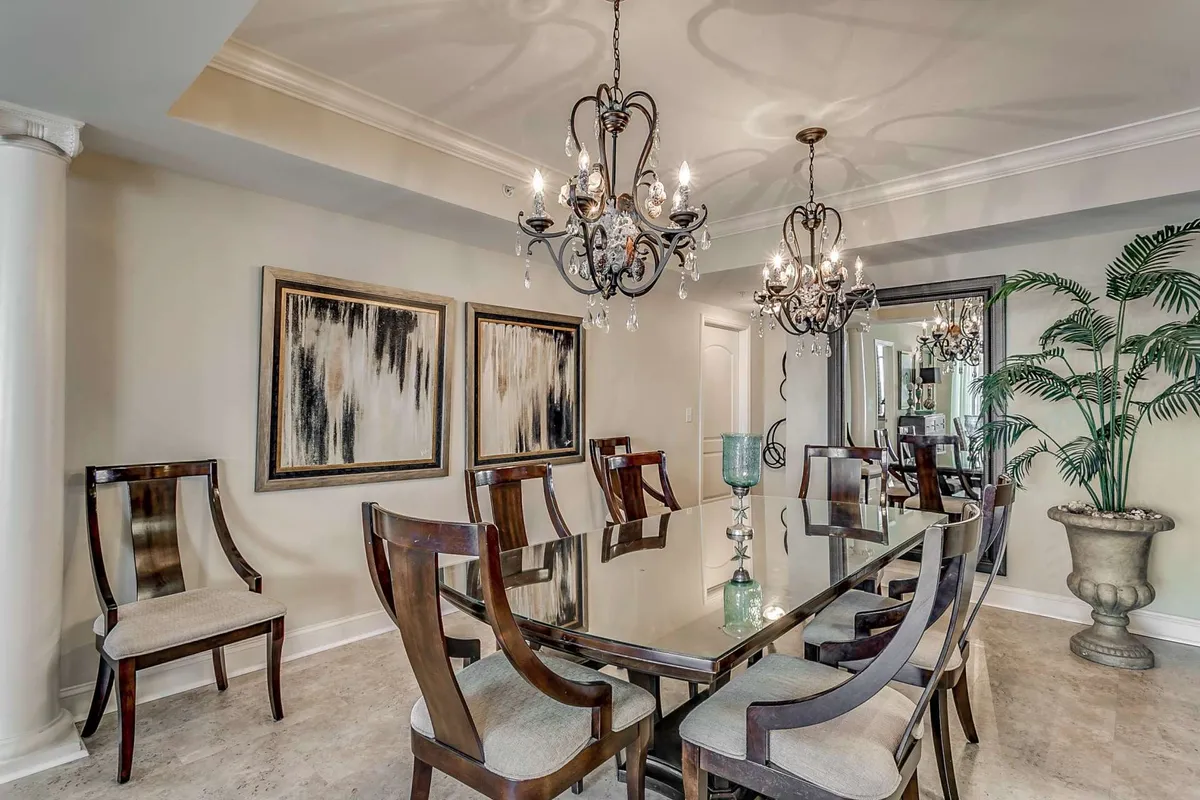 This image depicts a bright, sophisticated dining space with a glass table, modern chandeliers, lively artwork, and lush indoor plants. The setting is ideal for group gatherings, dinners, and celebrations, highlighting the elegant yet welcoming ambiance of the condo’s main living area.