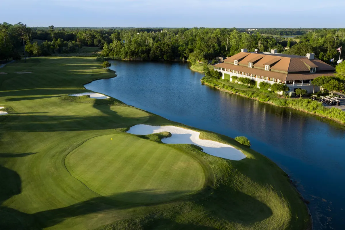 A lush, green golf course stretches into the distance, bordered by a peaceful water body and anchored by a welcoming clubhouse. The landscape is bathed in soft sunlight, suggesting a relaxing day outdoors. The scene exudes the leisurely pace and camaraderie of a day spent golfing with friends.