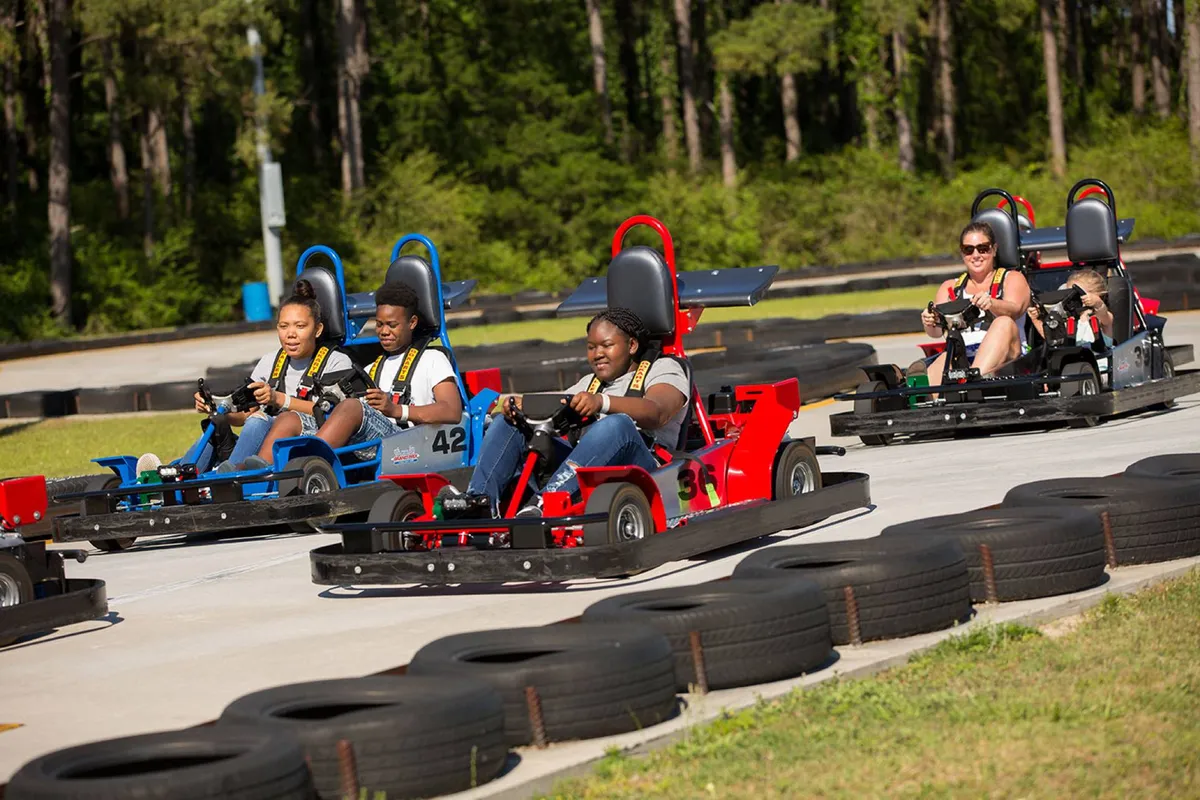 A thrilling exterior shot of a go-kart track with participants racing and spectators watching, capturing the exhilarating family activity available nearby. The scene is filled with motion, excitement, and the shared joy of outdoor recreation.