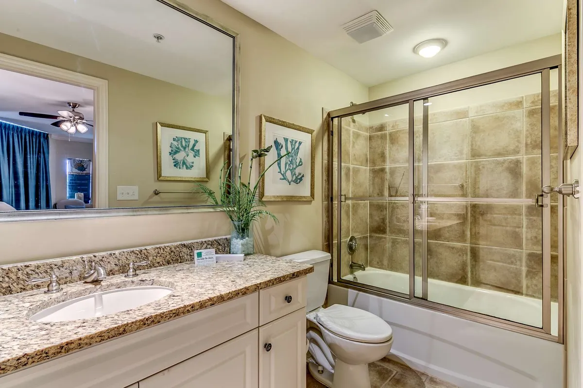 A modern bathroom with a granite countertop, elegant glass shower enclosure, and framed botanical artwork. The bathroom exudes a refreshing and tranquil vibe, suggesting an ideal spot for personal grooming and relaxation after a long day.